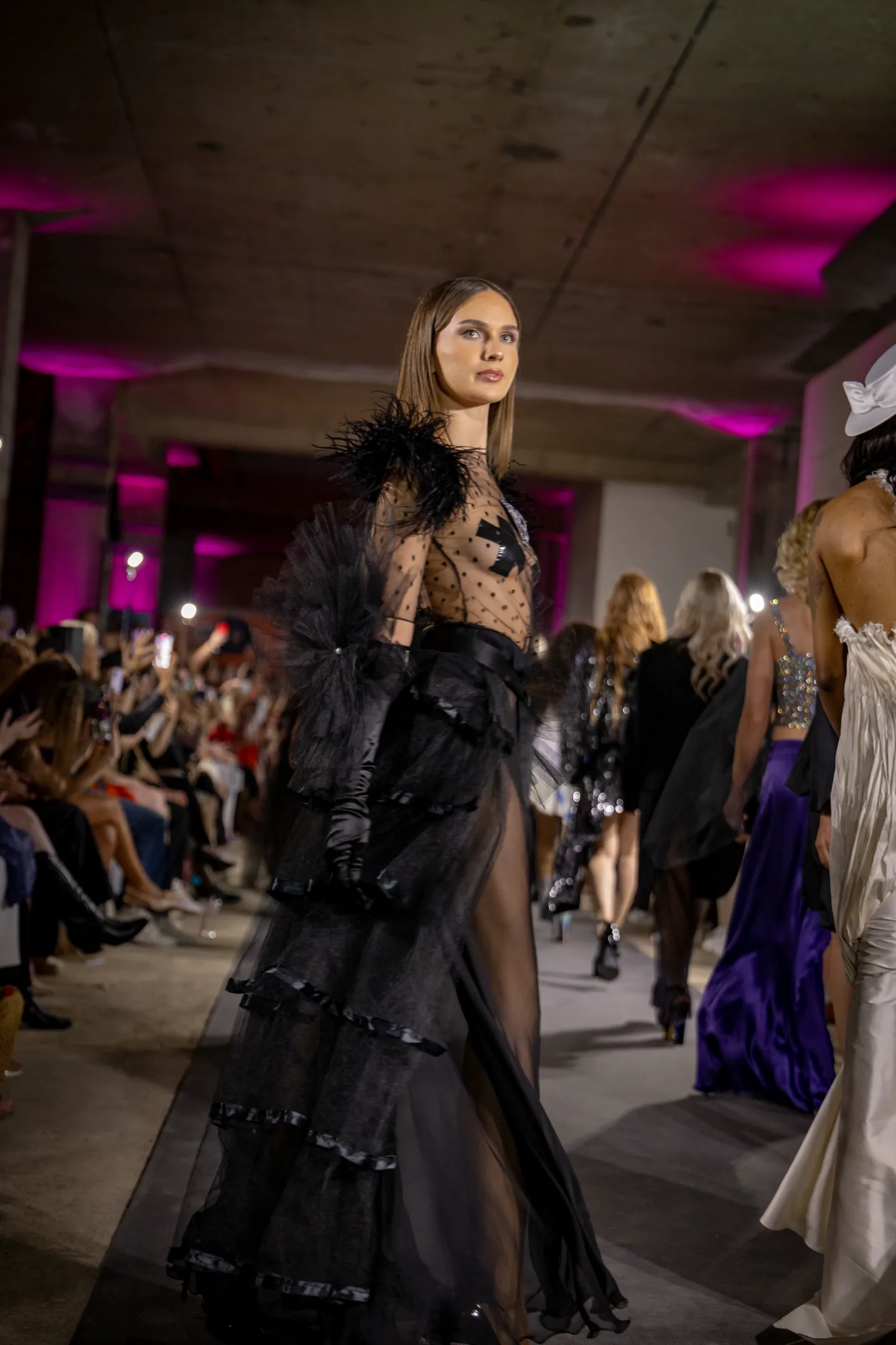 Sheer black couture look beside the runway audience.